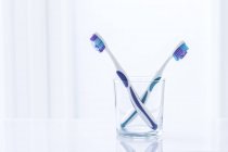 Purple toothbrushes in glass against plain background. — Stock Photo