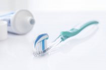 Toothbrush with white and blue toothpaste against white background. — Stock Photo