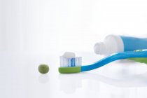 Cepillo de dientes con cantidad de pasta de dientes del tamaño de un guisante y tubo contra fondo blanco . - foto de stock