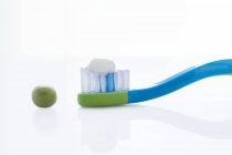 Cepillo de dientes con cantidad de pasta de dientes del tamaño de un guisante contra fondo blanco . - foto de stock