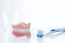 Dentures and toothbrush against white background, studio shot. — Stock Photo