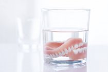 Prótesis dentales en vaso de agua sobre fondo blanco . - foto de stock