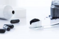 Holzkohle-Zahnpasta auf Zahnbürste mit schwarzen Kapseln, Studioaufnahme. — Stockfoto