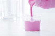 Medicina antiacida rosa versata nel bicchiere dosatore . — Foto stock
