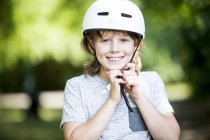 Junge befestigt Fahrradhelm im Park und lächelt. — Stockfoto
