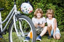 Jungen sitzen mit Handy auf Fahrrad mit Helm. — Stockfoto