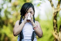 Elementary idade doente menina usando lenço enquanto espirra ao ar livre . — Fotografia de Stock