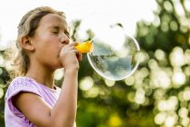 Pre-adolescent girl blowing bubbles with bubble wand in park. — Stock Photo