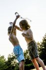 Хлопці ллють воду один на одного з пластикової пляшки і сміються в парку . — стокове фото