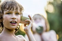Close-up of elementary age boy playing with tin can telephone. — Stock Photo