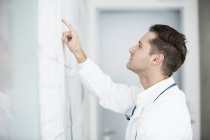 Vue latérale du médecin masculin adulte moyen inspectant le tableau blanc . — Photo de stock