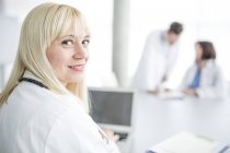Médica feminina olhando por cima do ombro e sorrindo no interior da clínica . — Fotografia de Stock