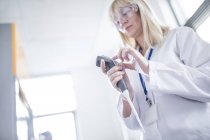 Visão de baixo ângulo da cientista feminina usando óculos de proteção e usando o dispositivo . — Fotografia de Stock