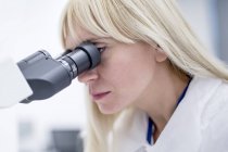 Женщина-лаборант, использующая микроскоп в лаборатории . — стоковое фото