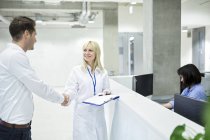 Female doctor shaking hands with male patient at hospital desk. — Stock Photo