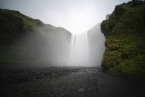 Nevoeiro sobre a água corrente da cachoeira Skogafoss, Islândia . — Fotografia de Stock