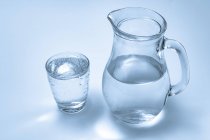 Glass and jug of mineral water on plain background. — Stock Photo