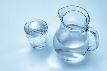 Bicchiere e brocca di acqua minerale su fondo chiaro . — Foto stock