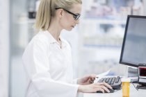 Жінка-фармацевт, що працює на комп'ютері в аптеці . — стокове фото