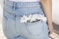 Vista cortada de mulher com flores brancas no bolso traseiro de jeans . — Fotografia de Stock