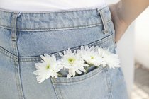 Обрезанный вид женщины с белыми цветами в заднем кармане джинсов . — стоковое фото