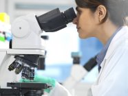 Cientista que vê a amostra médica na corrediça de vidro sob o microscópio no laboratório . — Fotografia de Stock