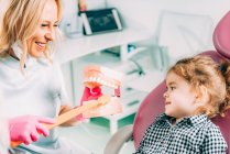 Petite fille à la clinique dentaire apprendre à se brosser les dents correctement avec orthodontiste femelle . — Photo de stock