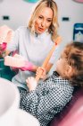 Little girl at dental clinic learning brushing teeth correctly with female orthodontist. — Stock Photo