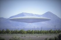 Composite image of unidentified flying object flying over plantation with mountains behind. — Stock Photo