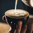 Profesional barista verter leche al vapor en la taza de café haciendo hermoso arte latte patrón Rosetta . - foto de stock