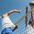 Низкий угол обзора игроков в пляжный волейбол, ударяющих мячом по сетке . — стоковое фото