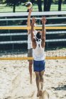 Joueurs de volley-ball de plage bloquant au filet pendant le match . — Photo de stock