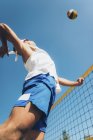 Low angle view of beach volleyball player jumping for ball at net. — Stock Photo