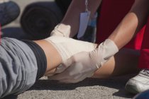 Nahaufnahme der Hände eines Sanitäters, der eine Knieverletzung mit einem Verband behandelt. — Stockfoto