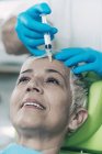 Mature woman receiving botox injection in forehead in cosmetology clinic. — Stock Photo