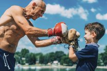 Grandfather and grandson boxing by lake outdoors. — Stock Photo
