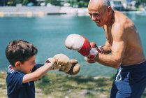Abuelo y nieto boxeando junto al lago al aire libre . - foto de stock