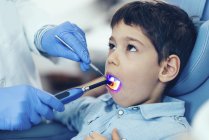 Relleno del ajuste del dentista con luz UV mientras examina a un paciente de edad elemental . - foto de stock