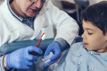 Dentist teaching elementary age boy about dental hygiene with brush and jaw model. — Stock Photo