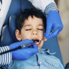 Hands of dentist drilling elementary age boy teeth. — Stock Photo