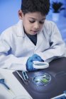 Schoolboy examining leaves with magnifying glass in school laboratory. — Stock Photo