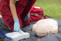 Un ambulancier paramédical féminin utilise un défibrillateur portatif pendant un entraînement de RCR à l'extérieur . — Photo de stock