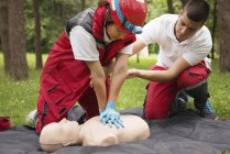 Entrenamiento de RCP paramédica femenina en maniquí con instructor al aire libre
. - foto de stock