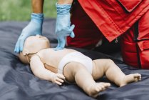 Manos del entrenamiento de RCP paramédico femenino en maniquí de bebé al aire libre . - foto de stock