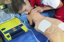 Female paramedic CPR training with defibrillator and dummy. — Stock Photo