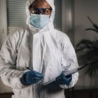 Forensics expert in protective suit writing in clipboard while examining crime scene. — Stock Photo