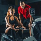 Fit woman with male instructor performing rowing machine workout. — Stock Photo