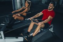 Fit woman and man performing rowing machine workout in gym. — Stock Photo