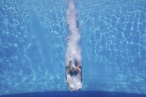 Buzo hembra nadando con salpicaduras bajo el agua después de saltar en la piscina . - foto de stock