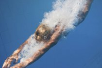 Mergulhador feminino nadando com salpicos subaquáticos após salto atlético na piscina . — Fotografia de Stock